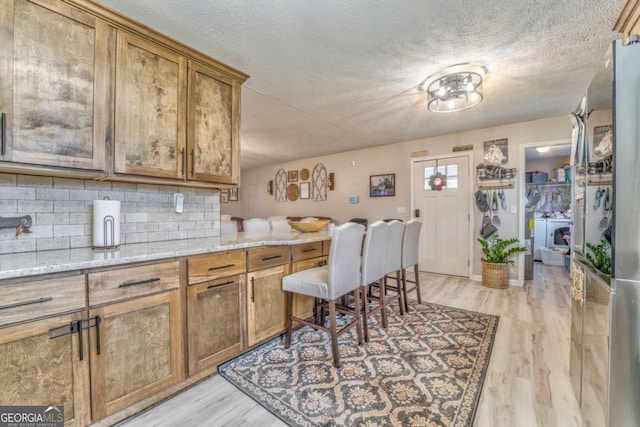 kitchen featuring light stone counters, washing machine and dryer, decorative backsplash, and light wood-type flooring