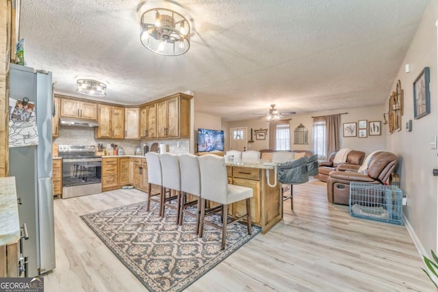 kitchen featuring appliances with stainless steel finishes, a breakfast bar, decorative backsplash, kitchen peninsula, and light wood-type flooring