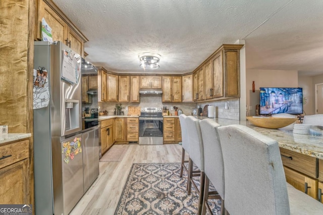 kitchen featuring light hardwood / wood-style flooring, backsplash, stainless steel appliances, light stone countertops, and a textured ceiling