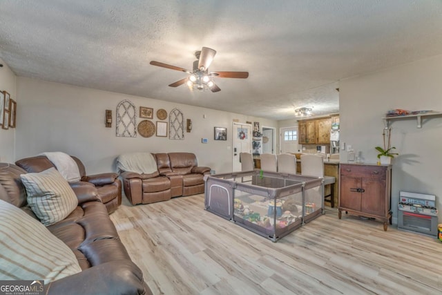 living room featuring ceiling fan, a textured ceiling, and light hardwood / wood-style floors