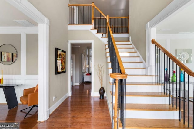 stairway featuring a high ceiling, ornamental molding, and hardwood / wood-style floors