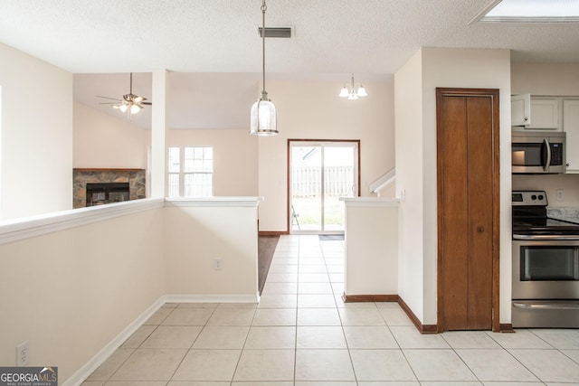 kitchen featuring light tile patterned floors, a premium fireplace, white cabinetry, hanging light fixtures, and stainless steel appliances