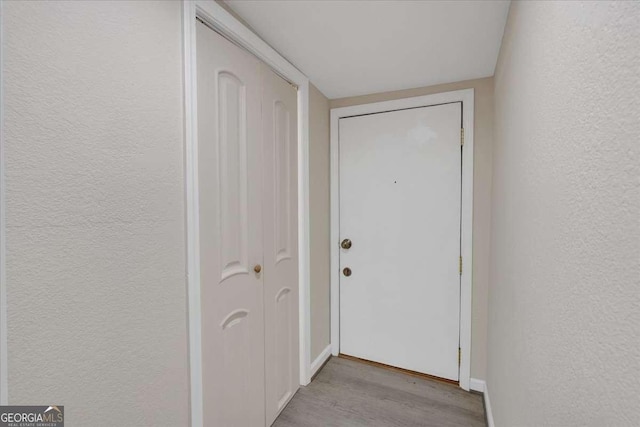 entryway featuring baseboards, light wood finished floors, and a textured wall