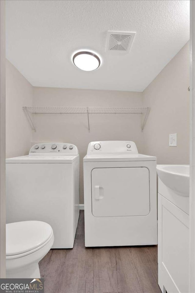 laundry room with washing machine and dryer, visible vents, a sink, wood finished floors, and laundry area
