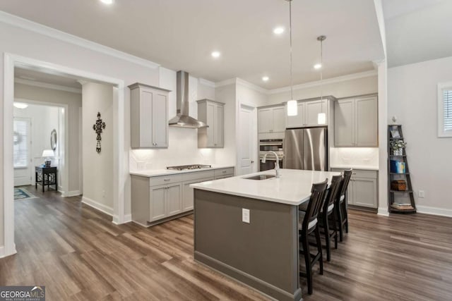 kitchen featuring appliances with stainless steel finishes, pendant lighting, an island with sink, gray cabinetry, and wall chimney exhaust hood