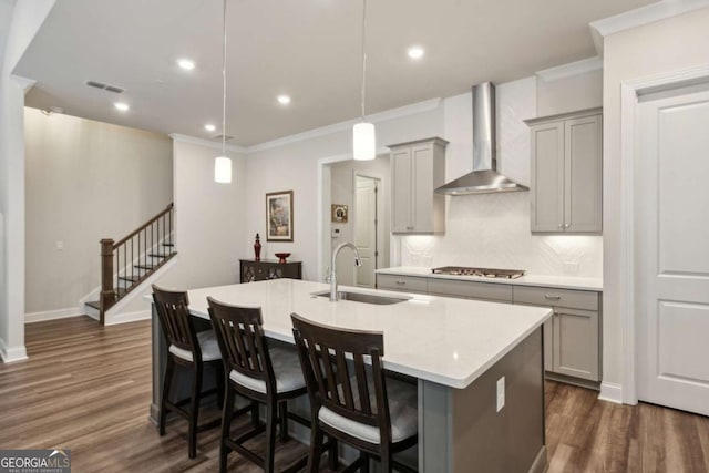 kitchen with wall chimney exhaust hood, sink, decorative light fixtures, a center island with sink, and stainless steel gas stovetop