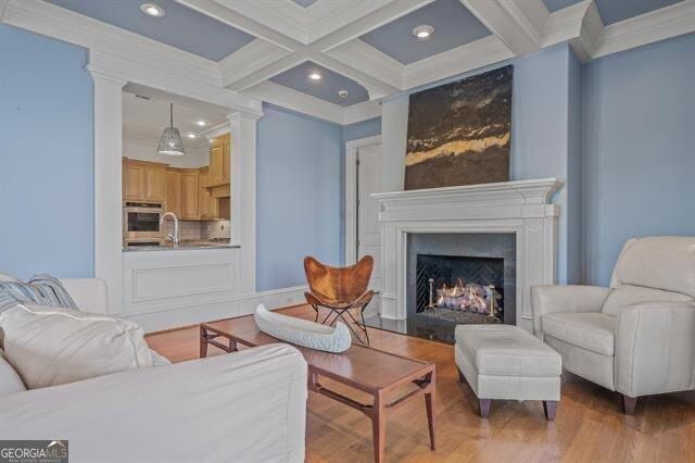 living room with beamed ceiling, coffered ceiling, sink, and light hardwood / wood-style flooring