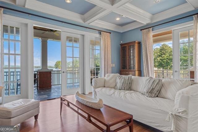 living room with beamed ceiling, wood-type flooring, ornamental molding, coffered ceiling, and ceiling fan