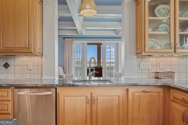 kitchen featuring sink, dishwasher, decorative columns, coffered ceiling, and dark stone counters