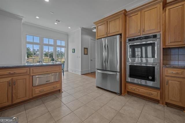 kitchen featuring light tile patterned floors, decorative backsplash, ornamental molding, and stainless steel appliances