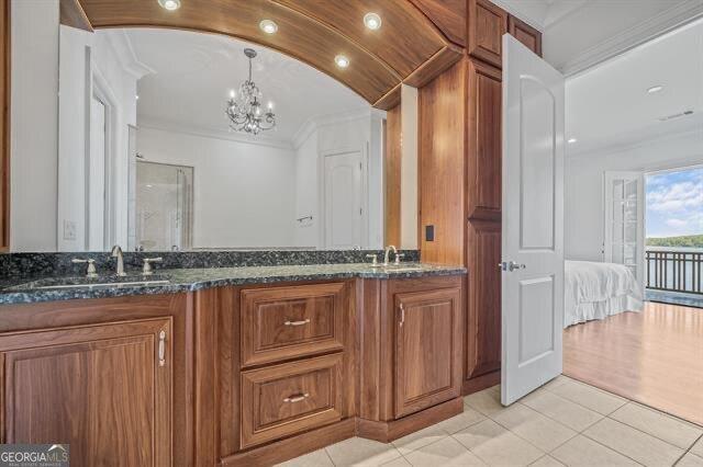 bathroom with vaulted ceiling, vanity, ornamental molding, tile patterned floors, and an inviting chandelier