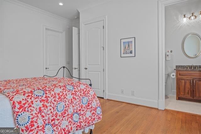 bedroom with sink, light hardwood / wood-style flooring, ornamental molding, and ensuite bathroom