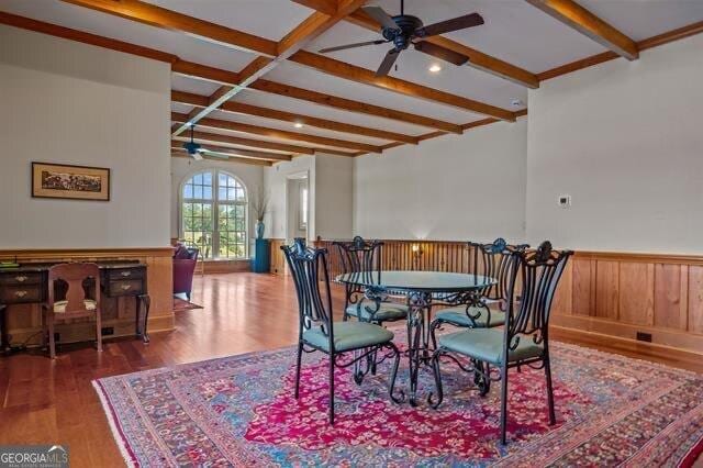 dining space featuring beam ceiling, wood-type flooring, ceiling fan, and wood walls