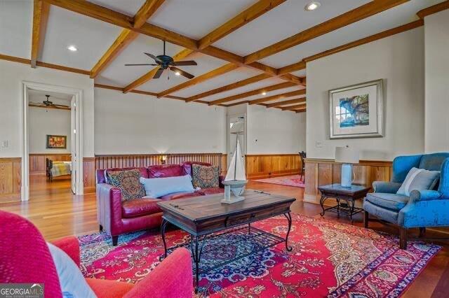 living room with beamed ceiling, ceiling fan, wood-type flooring, and wood walls