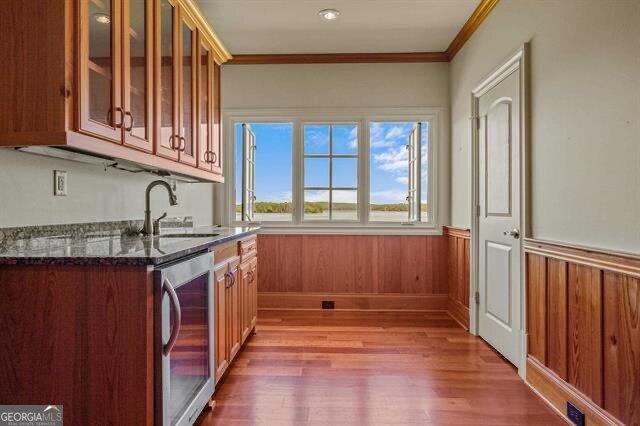 kitchen with sink, crown molding, hardwood / wood-style flooring, dark stone counters, and beverage cooler