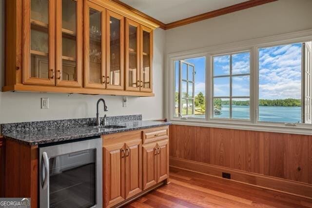 kitchen featuring sink, wine cooler, dark stone counters, crown molding, and a water view