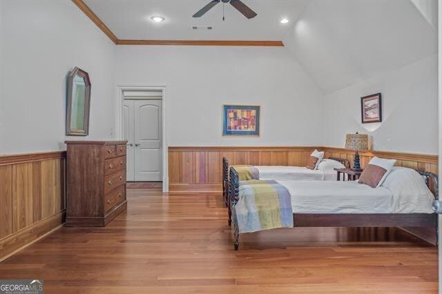 bedroom featuring lofted ceiling, hardwood / wood-style floors, wooden walls, and ceiling fan