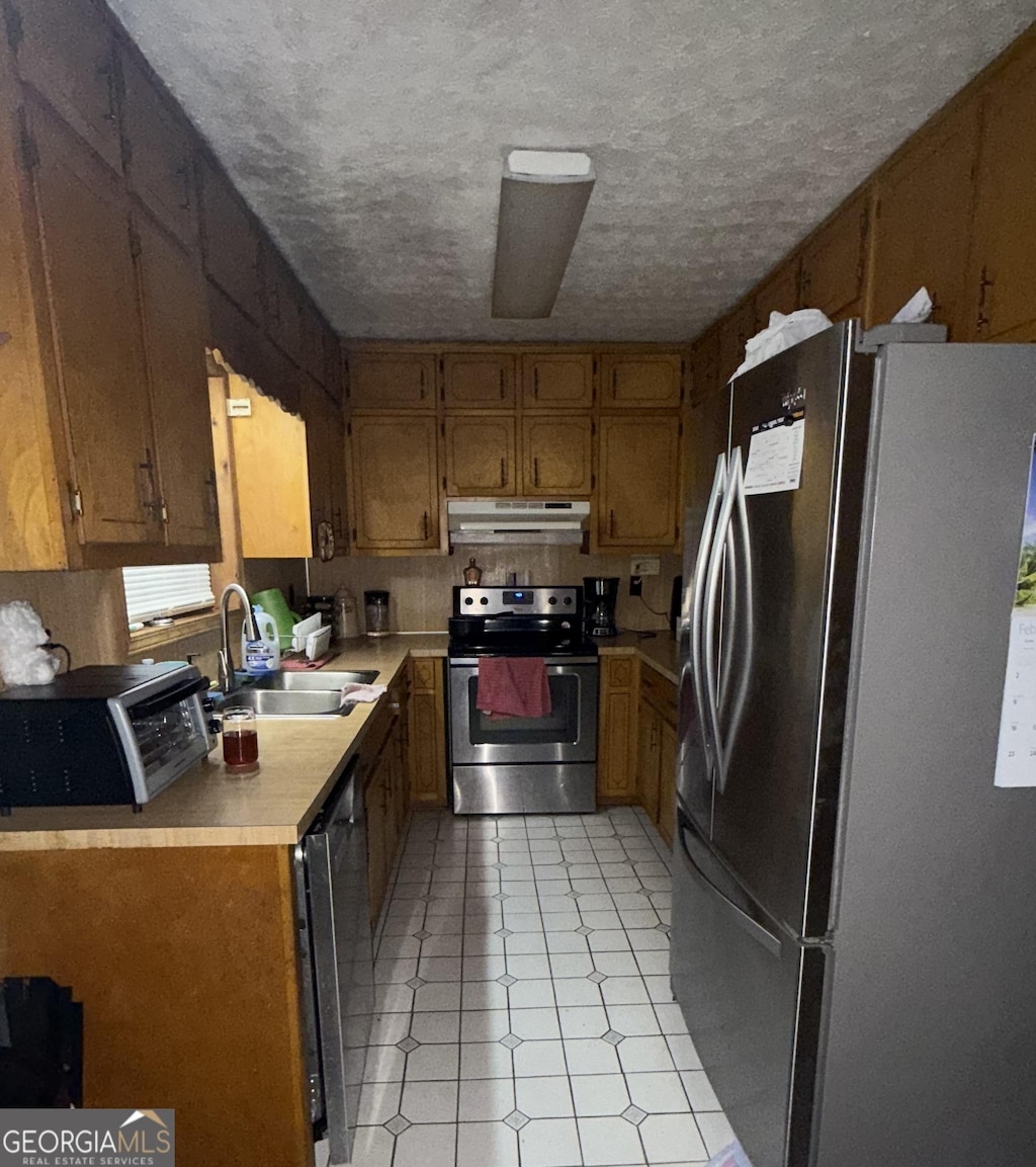 kitchen featuring sink, light tile patterned floors, stainless steel appliances, and a textured ceiling