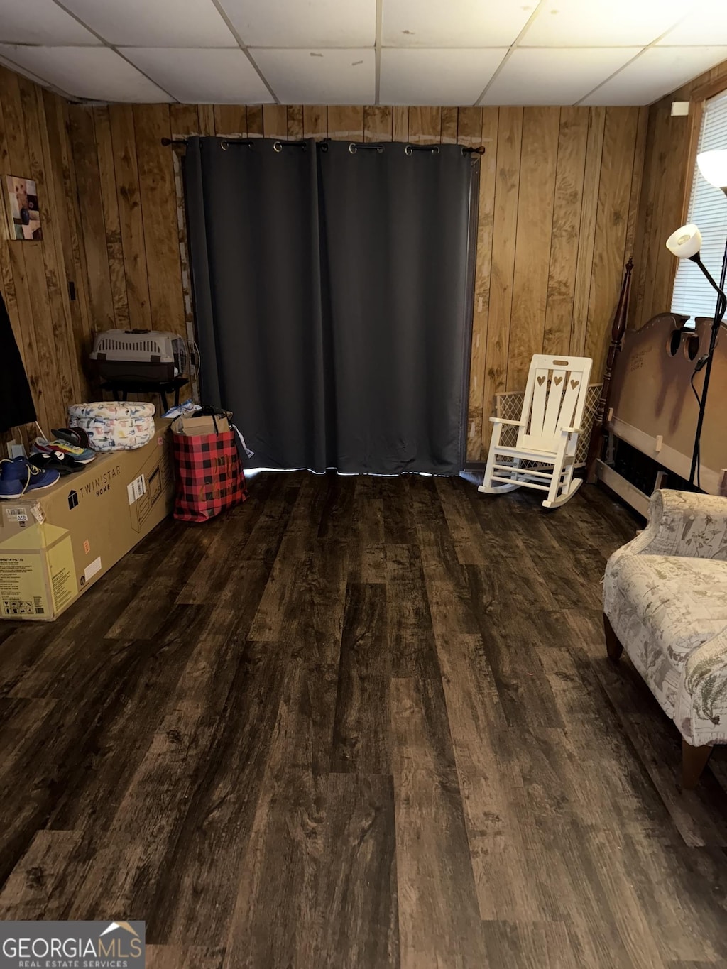 living area with a drop ceiling, dark hardwood / wood-style floors, and wood walls