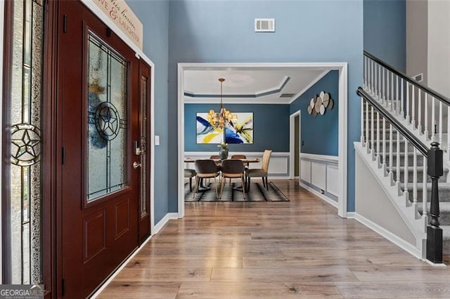 foyer featuring an inviting chandelier, a tray ceiling, light hardwood / wood-style floors, and crown molding