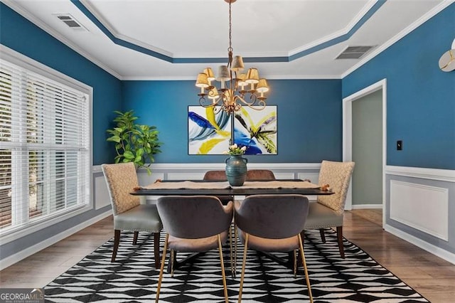 dining area featuring hardwood / wood-style flooring, ornamental molding, a tray ceiling, and a notable chandelier