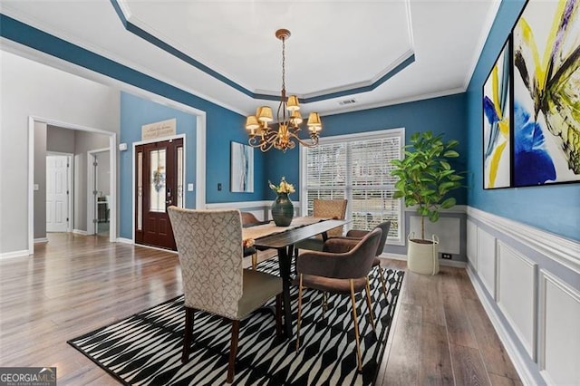 dining area featuring a raised ceiling, ornamental molding, hardwood / wood-style flooring, and a chandelier