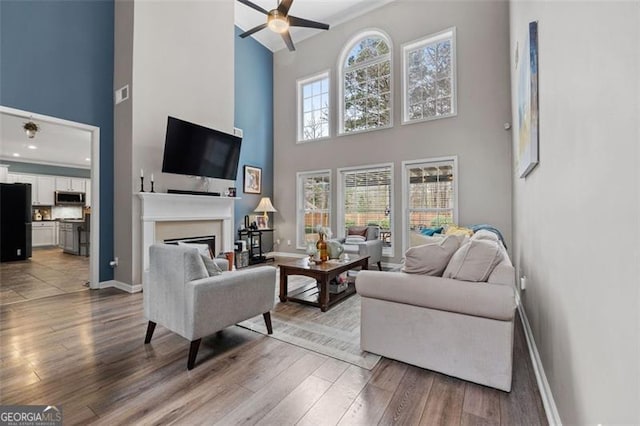 living room with a high ceiling, ceiling fan, and light hardwood / wood-style floors