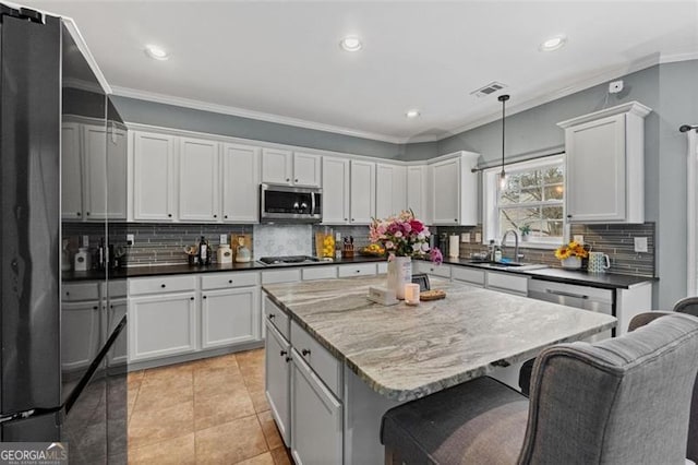 kitchen featuring sink, white cabinetry, stainless steel appliances, a kitchen island, and decorative light fixtures