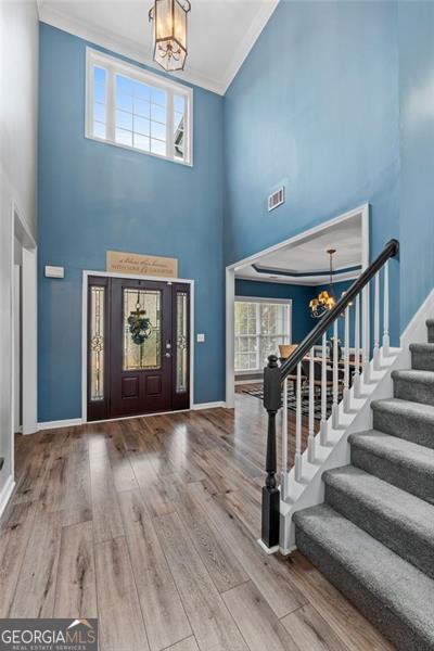 foyer entrance with wood-type flooring, ornamental molding, a chandelier, and a towering ceiling