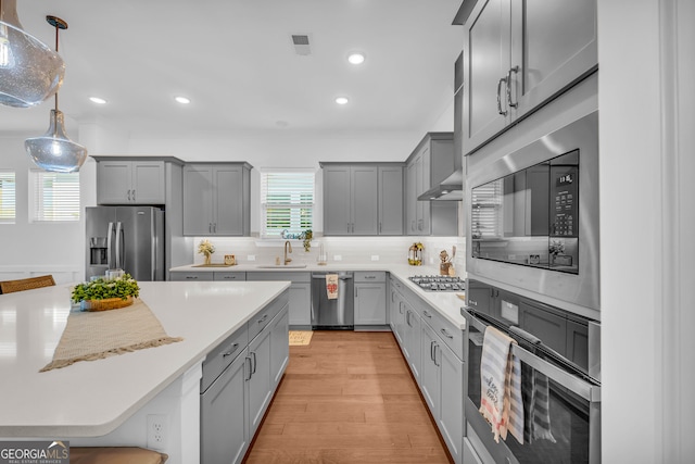 kitchen with decorative light fixtures, tasteful backsplash, sink, gray cabinetry, and stainless steel appliances