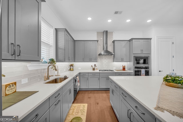 kitchen with gray cabinetry, sink, wall chimney exhaust hood, and appliances with stainless steel finishes