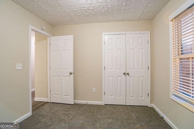 unfurnished bedroom with a textured ceiling, dark carpet, and a closet