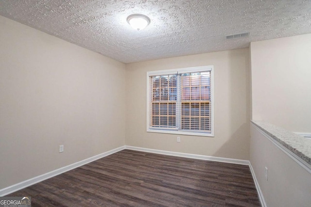 empty room with dark wood-type flooring and a textured ceiling