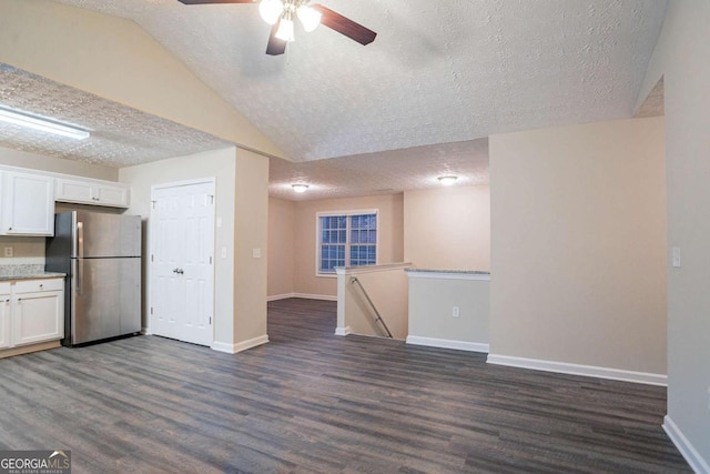 kitchen with dark wood-type flooring, stainless steel refrigerator, white cabinetry, a textured ceiling, and vaulted ceiling