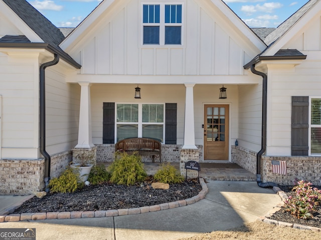 view of exterior entry with covered porch, board and batten siding, and brick siding