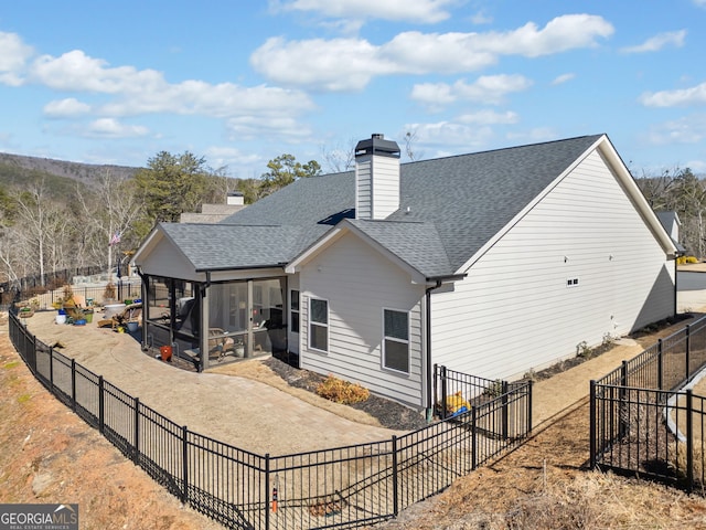 back of property with a fenced backyard, a chimney, a shingled roof, and a sunroom