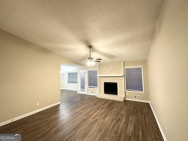 unfurnished living room featuring a stone fireplace, lofted ceiling, ceiling fan, dark wood-type flooring, and a textured ceiling