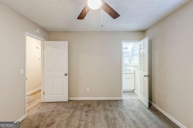 unfurnished bedroom with ceiling fan, ensuite bath, light colored carpet, and a textured ceiling