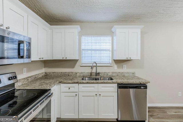 kitchen featuring stainless steel appliances, sink, white cabinets, and light stone counters