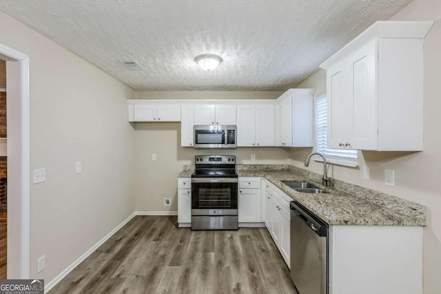 kitchen with stainless steel appliances, white cabinetry, light stone countertops, and sink