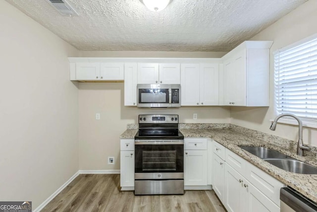 kitchen featuring stainless steel appliances, white cabinetry, sink, and light wood-type flooring