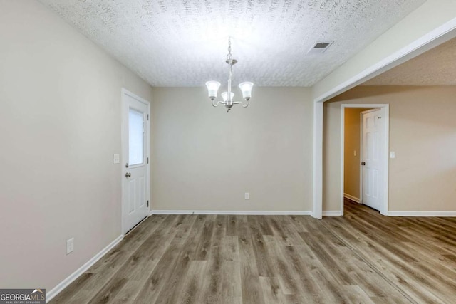 unfurnished dining area featuring a chandelier, a textured ceiling, and light wood-type flooring