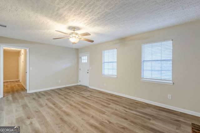 empty room with ceiling fan, a textured ceiling, and light wood-type flooring