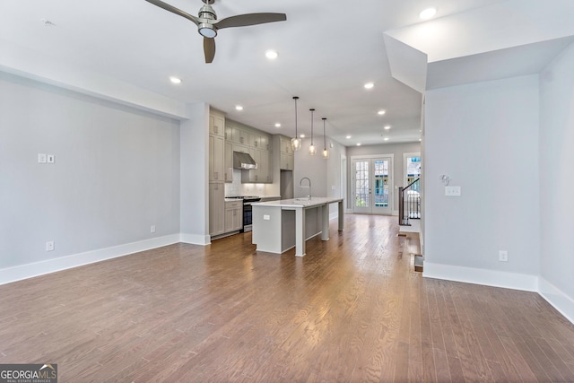 unfurnished living room featuring dark hardwood / wood-style floors, pendant lighting, sink, a breakfast bar area, and a center island with sink