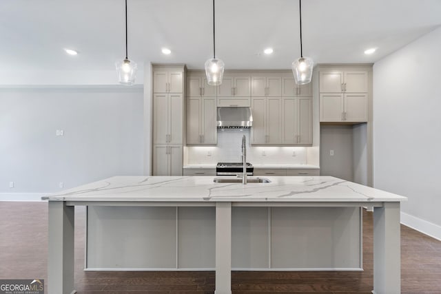 kitchen with pendant lighting, ventilation hood, tasteful backsplash, a large island with sink, and light stone countertops