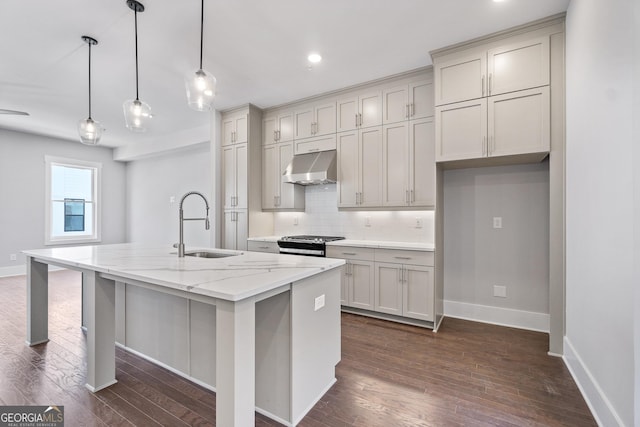 kitchen featuring stainless steel stove, decorative light fixtures, sink, a kitchen island with sink, and light stone counters