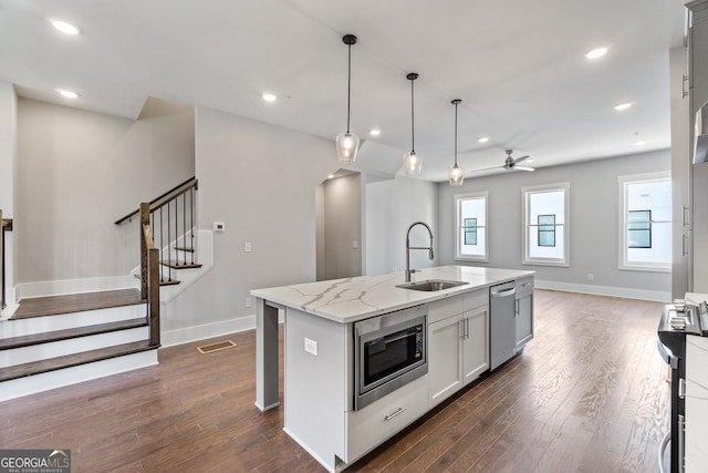 kitchen featuring sink, stainless steel appliances, light stone countertops, an island with sink, and decorative light fixtures