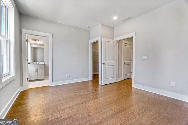 unfurnished bedroom with baseboards, connected bathroom, visible vents, and wood finished floors