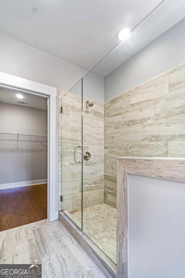 full bathroom with a shower stall, a walk in closet, and wood finished floors