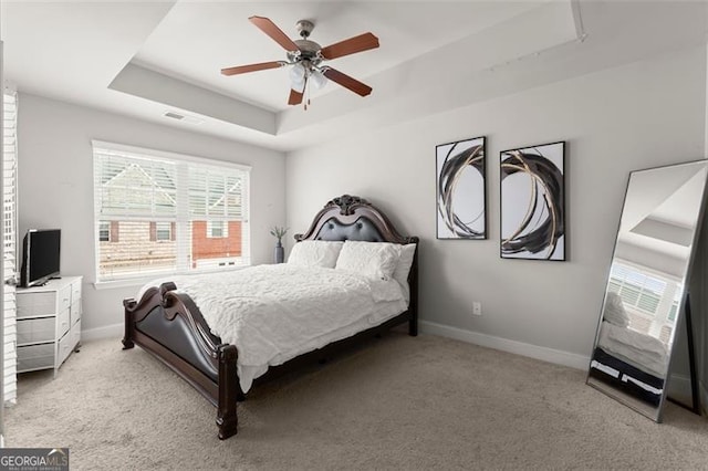 carpeted bedroom with a tray ceiling and ceiling fan